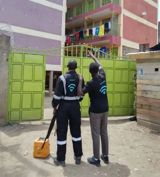 Two konnekt technicians at the gate of a multi-storey apartment block, surveying it for fibre